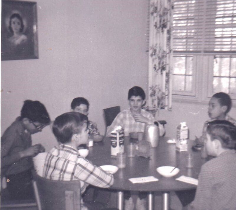 A group of children sitting around a table with drinks and napkins, in a room with curtains and Donnellan's diaries hanging on the wall.
