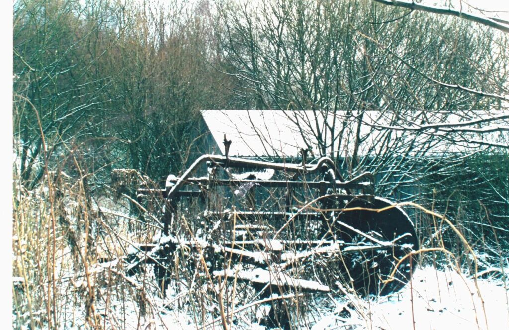 A rusted tractor sitting in the snow near trees.