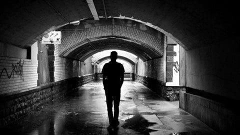 A man is standing in the middle of an empty tunnel.