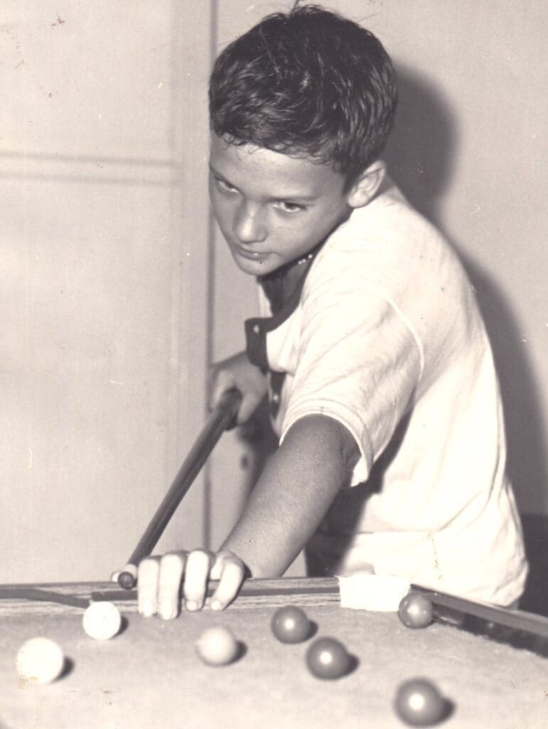 A young man playing pool in an old photo.