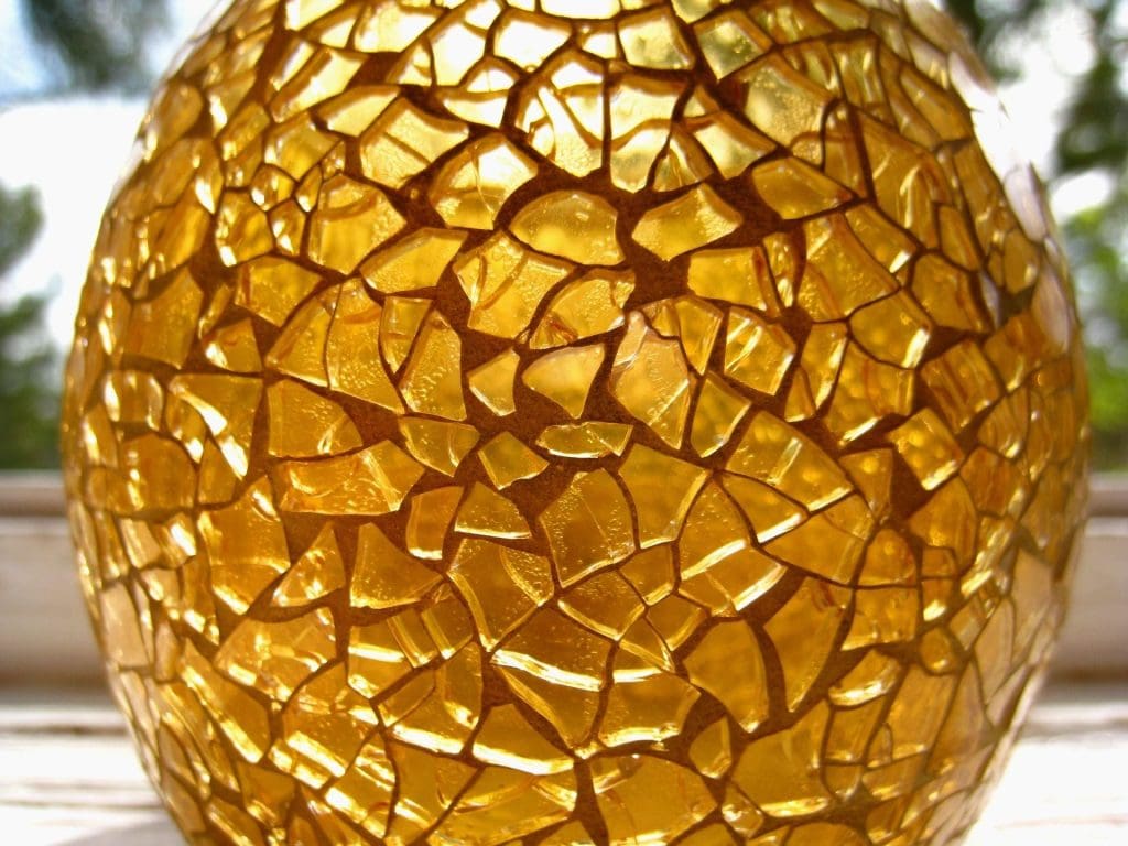 A close-up of a mosaic glass sphere with golden-yellow tones illuminated from within.