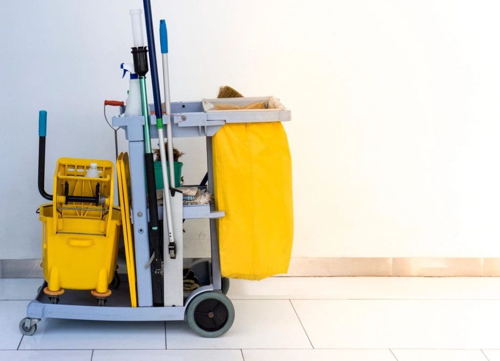 Janitorial cart with cleaning equipment and supplies against a white wall.