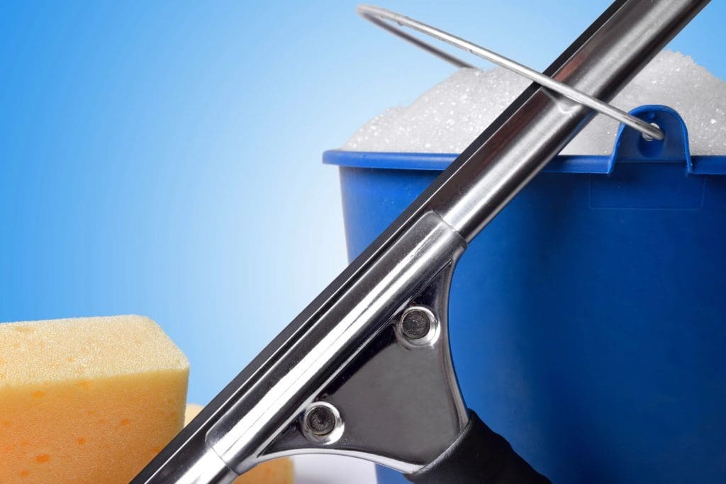 Close-up of cleaning supplies with a mop, bucket of soapy water, and sponge on a blue background.