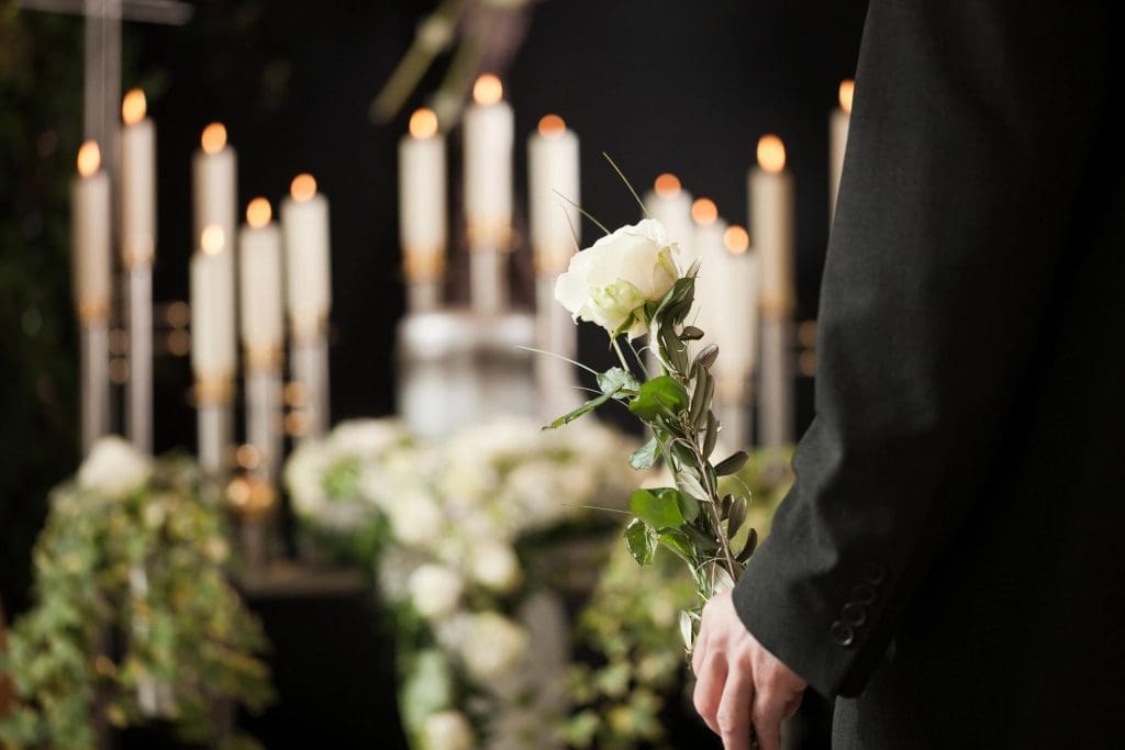 A person in formal attire with a boutonniere, standing beside a candlelit floral arrangement.