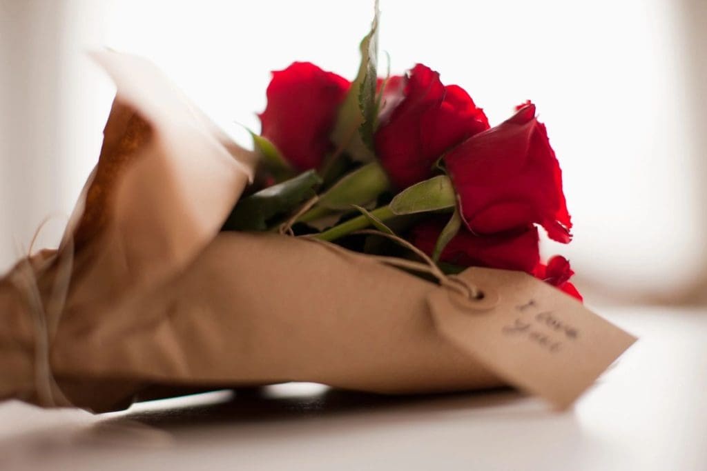 A bouquet of red roses wrapped in brown paper with a tag attached.